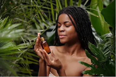 A female influencer with long hair examines a small amber bottle among lush green foliage, conveying a natural and serene vibe. She appears focused and content.